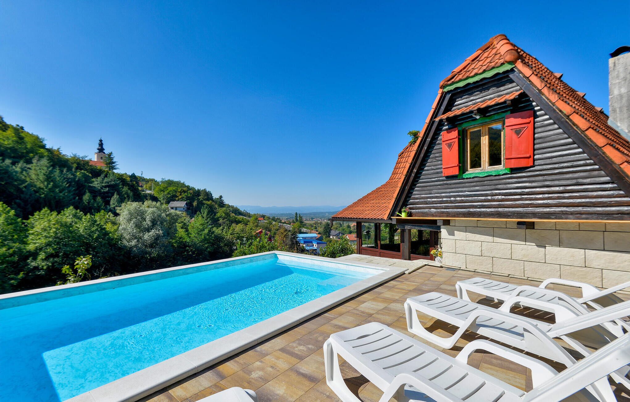 A poolside area with a wooden house, a clear blue sky, and a view of the landscape.