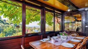 Un comedor con una mesa de madera dispuesta para cuatro, ventanas amplias con vistas a una ladera boscosa y un techo rústico con vigas a la vista.