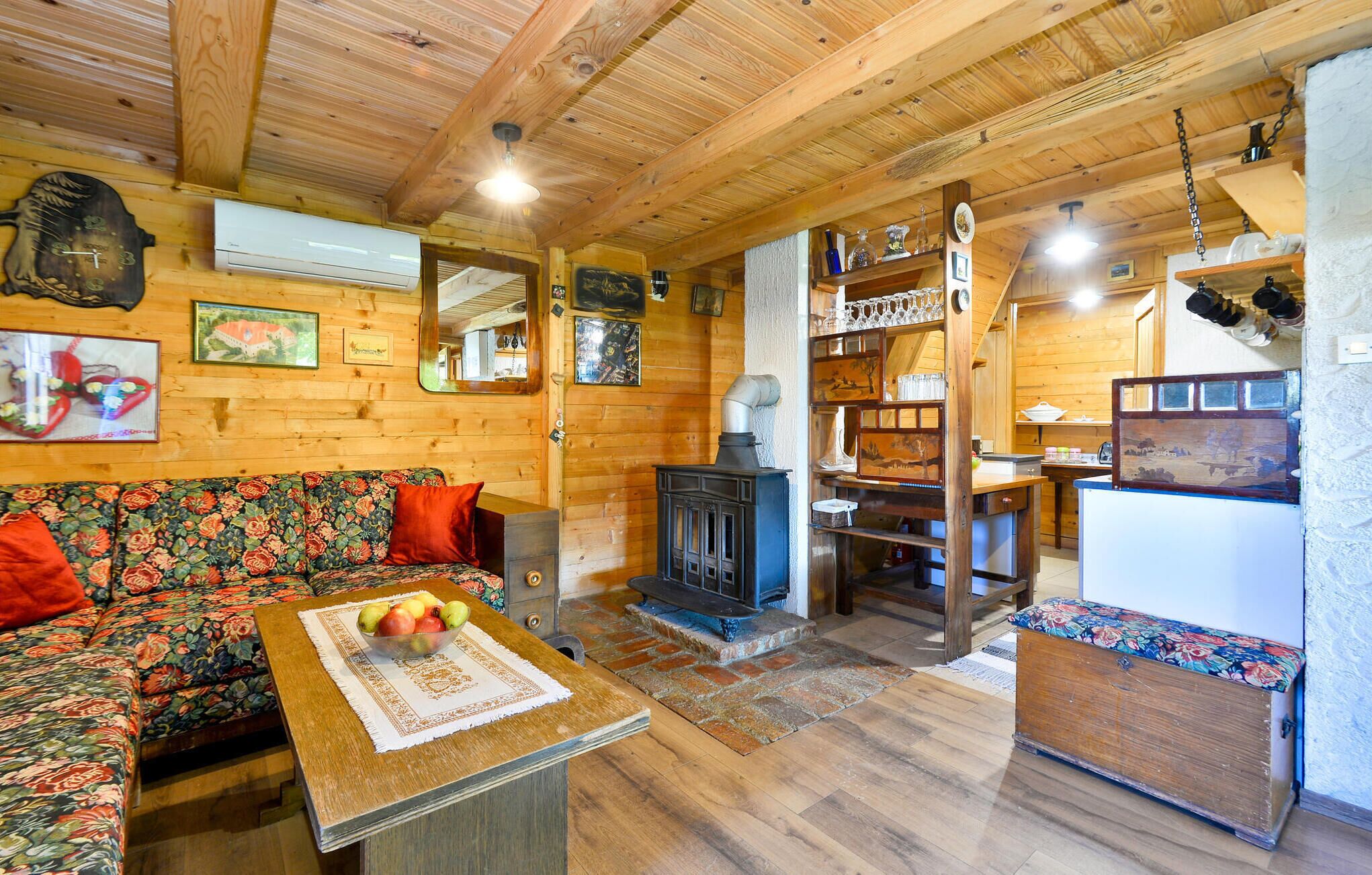 A cozy wooden cabin interior with a sofa, a table with fruit, a fireplace, and shelves with various items.