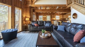 A spacious living room with a leather sofa, ottoman, and a wooden coffee table. - ❤️ of Hocking Hills 🌲 Hot Tub, Wifi, Close to Trails + Caves, 11 Secluded Acres (South Bloomingville)