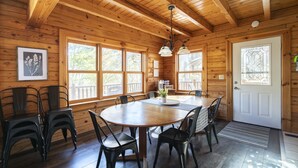 A wooden cabin interior with a round dining table, chairs, and a chandelier. - ❤️ of Hocking Hills 🌲 Hot Tub, Wifi, Close to Trails + Caves, 11 Secluded Acres (South Bloomingville)