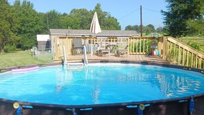 Une piscine ronde, installée à l’extérieur et hors sol, avec une terrasse en bois et un petit abri de jardin en arrière-plan.