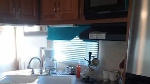 Une cuisine de taille réduite, dotée de meubles de rangement en bois, d’une cuisinière, d’un évier et d’un four à micro-ondes.