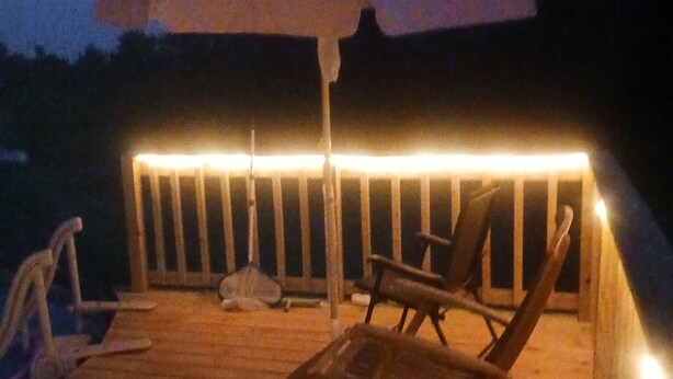 Une terrasse en bois avec une rambarde, deux chaises longues et un grand parasol pour créer de l’ombre.
