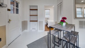 Un couloir moderne et bien éclairé, avec une porte blanche, une petite table entourée de chaises et une plante en pot.