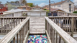Un escalier en bois mène à une terrasse, et des morceaux de tissu aux couleurs vives sont éparpillés en bas.