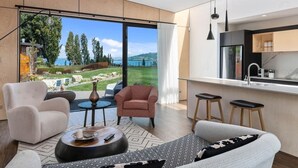 A modern living room with a large window, a sofa, a chair, and a coffee table. - Toka Ridge 1bd Lake View Lux Villa w/ HotTub (Hamurana)