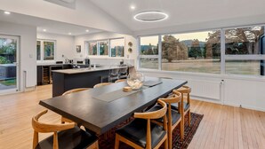 A modern kitchen with a central island, large windows, and a dining area with a dark table and wooden chairs. - Above Par Golf Course Villa with Hot Tub 4bd3.5bth (Rotorua)