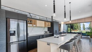 Een moderne keuken met een groot schiereiland, roestvrijstalen apparatuur en uitzicht op het groen.
