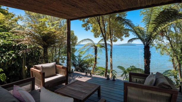 A covered outdoor seating area with wooden furniture and a view of the water. - Toka Ridge Lake View, Lux Villa 2bd2bth w/ HotTub (Hamurana)