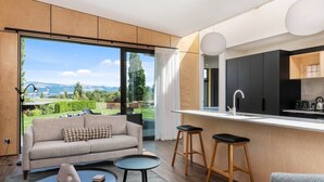 A modern kitchen with a large window, a sofa, two stools, and a small table. - Toka Ridge Lake View, Lux Villa 2bd2bth w/ HotTub (Hamurana)