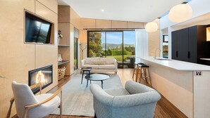 A modern kitchen with a large island, a dining area with a sofa and chairs, and a fireplace. - Toka Ridge Lake View, Lux Villa 2bd2bth w/ HotTub (Hamurana)