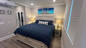A bedroom with a large bed, two bedside tables, a nightstand, a door, and a wall-mounted artwork.
