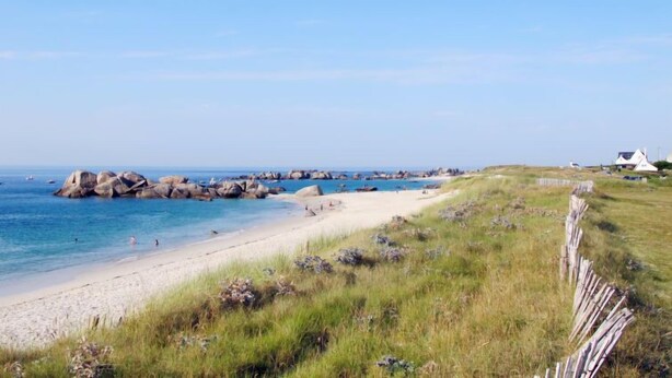 Un paisaje costero con una playa arenosa, afloramientos rocosos y algunas casas a lo lejos.