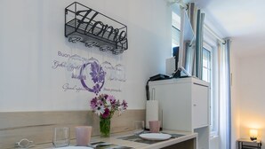 Cocina compacta con comedor, que incluye una encimera blanca, dos sillas, una mesa pequeña con un jarrón de flores y un estante en la pared sobre la encimera.