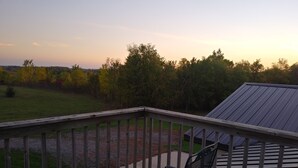 A wooden deck with a metal table and chairs, overlooking a grassy area with trees and a building with a metal roof. - Quiet, remotely located in the country. (Eden Valley)