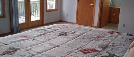 A bedroom with a large bed, a wooden door, and a balcony.