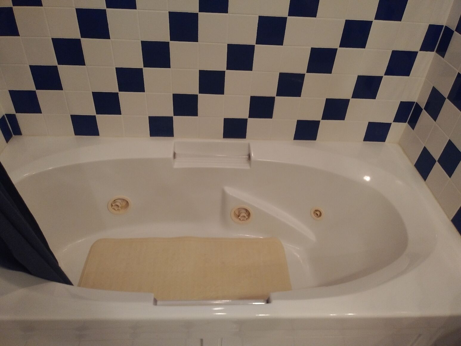 Een bad met een beige mat, omringd door blauw-witte betegelde vloertegels.