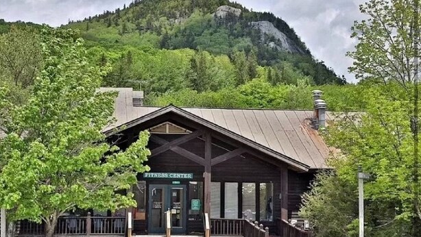 A rustic wooden building labeled "Fitness Center" with a porch and a mountain backdrop.