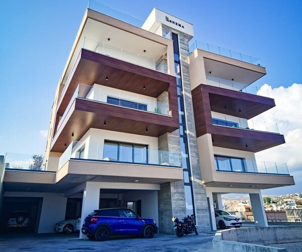 A multi-story residential building with a modern design, featuring balconies, large windows, and a garage with parked vehicles. - Brand NEW 2-Bed Apartment in Agios Athanasios (Agios Athanasios)