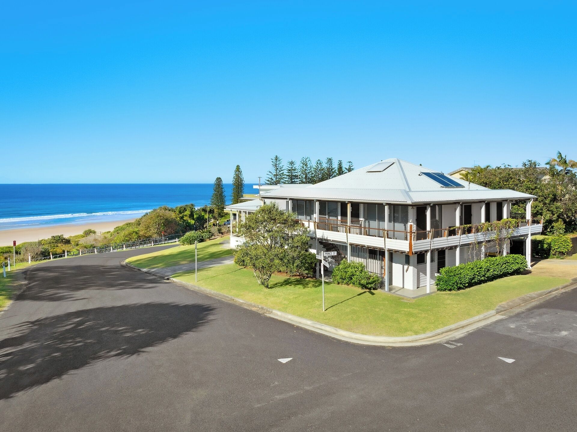 A two-story building with a balcony overlooking a beach, a clear sky, and a road leading to the building.
