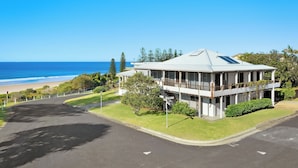 A two-story building with a balcony overlooking a beach, a clear sky, and a road leading to the building. - Spindrift Lowerdeck BEACH FRONT location! Retro style 2 bed, Wifi, Nespresso++++ (Yamba)
