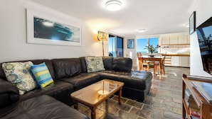 A living room with a leather sofa, a glass coffee table, and a dining area with a wooden table and chairs. - Spindrift Lowerdeck BEACH FRONT location! Retro style 2 bed, Wifi, Nespresso++++ (Yamba)