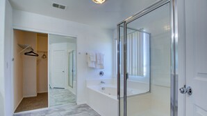 Une salle de bain moderne dotée d’une douche à parois de verre, d’une baignoire blanche et d’un dressing ouvert avec une tringle à vêtements.
