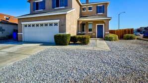 Une maison à deux étages avec un garage, une allée de gravier bien entretenue et des arbustes soigneusement taillés.