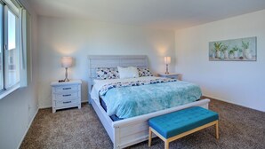 Une chambre à coucher comprenant un lit, des tables de chevet, un banc et un tableau accroché au mur.