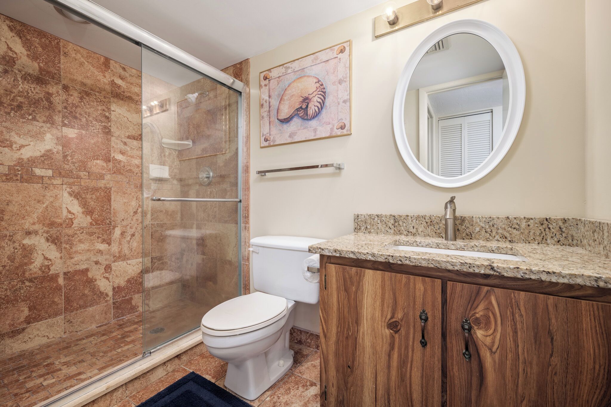 Een badkamer met een douchecabine van glas, een toilet, een houten wastafelmeubel met een wastafel en een spiegel aan de muur.