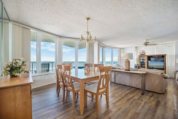 A spacious dining area with a large table and chairs, a chandelier, and a view of the ocean through large windows.