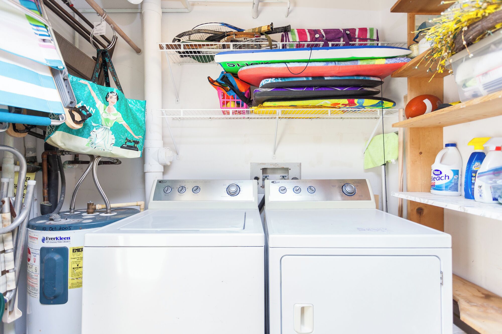 A laundry area with two white washing machines, a shelf with folded towels, and a rack with various items including a tennis racket.