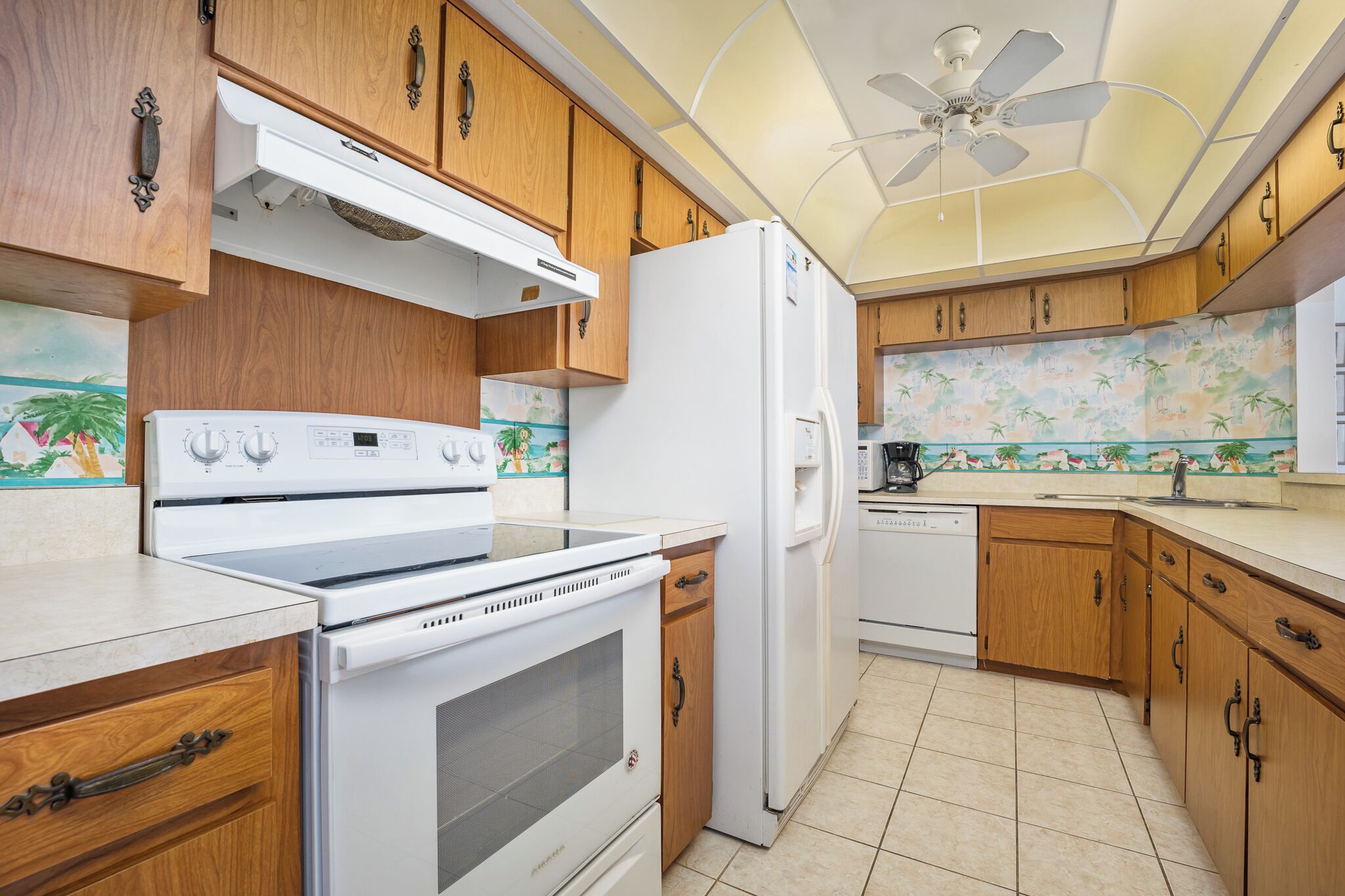 A kitchen with wooden cabinets, a white stove, a refrigerator, and a ceiling fan.