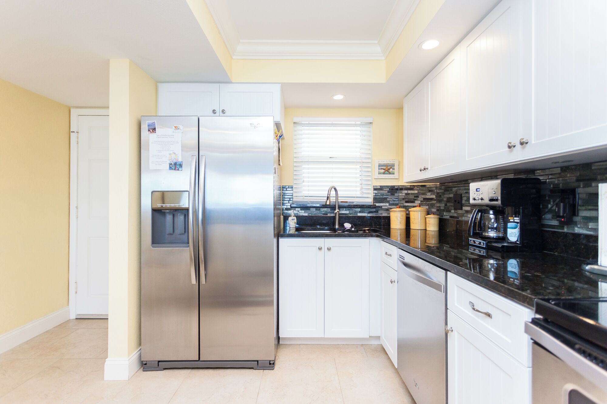 A modern kitchen with stainless steel appliances, white cabinetry, and a black countertop.