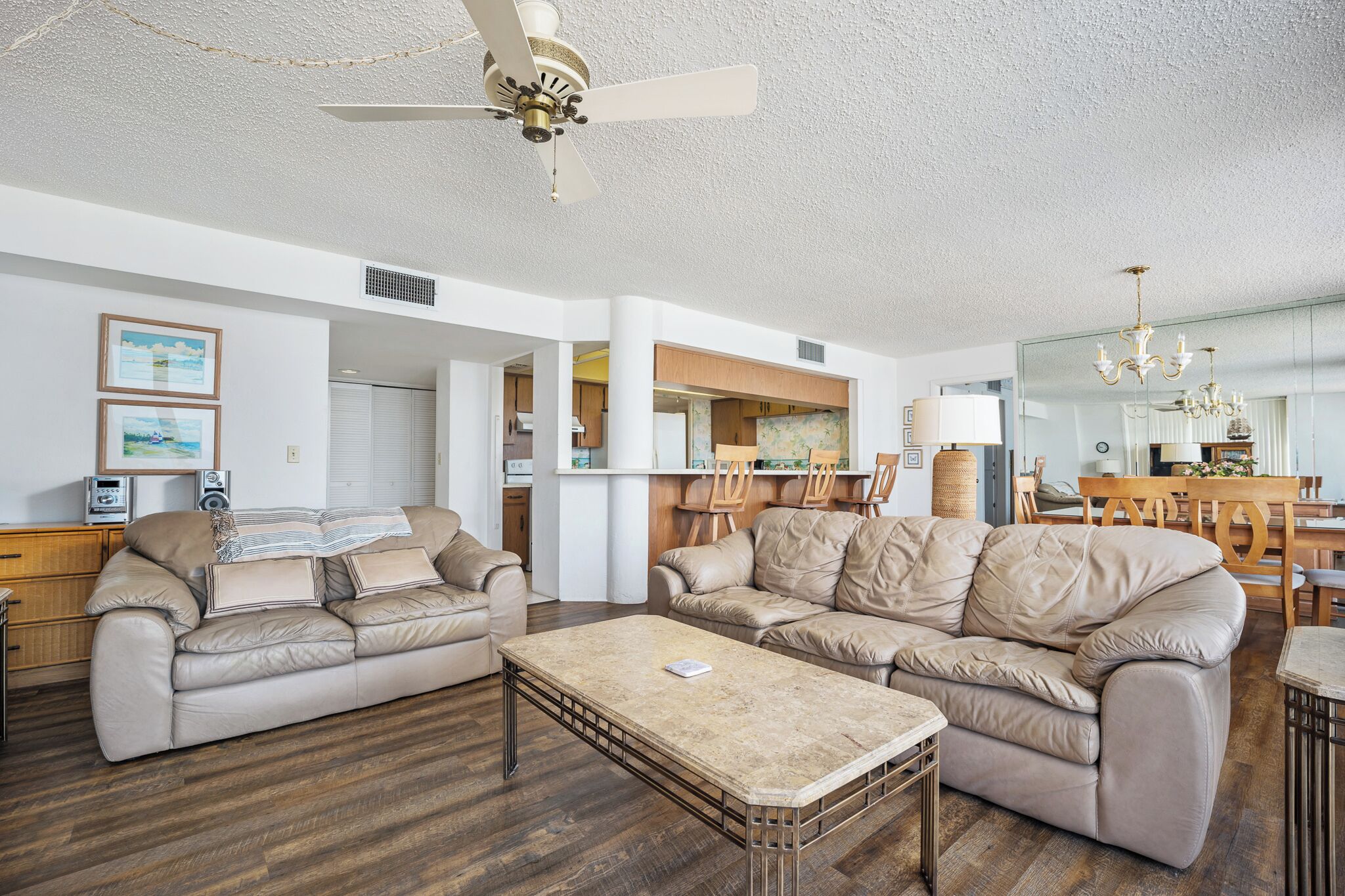 A spacious living room with two beige sofas, a coffee table, and a ceiling fan.