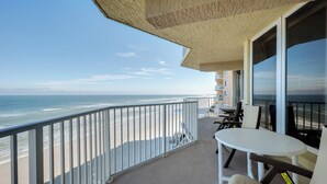 Un balcon donnant sur la plage, avec une table, des chaises et une rambarde.