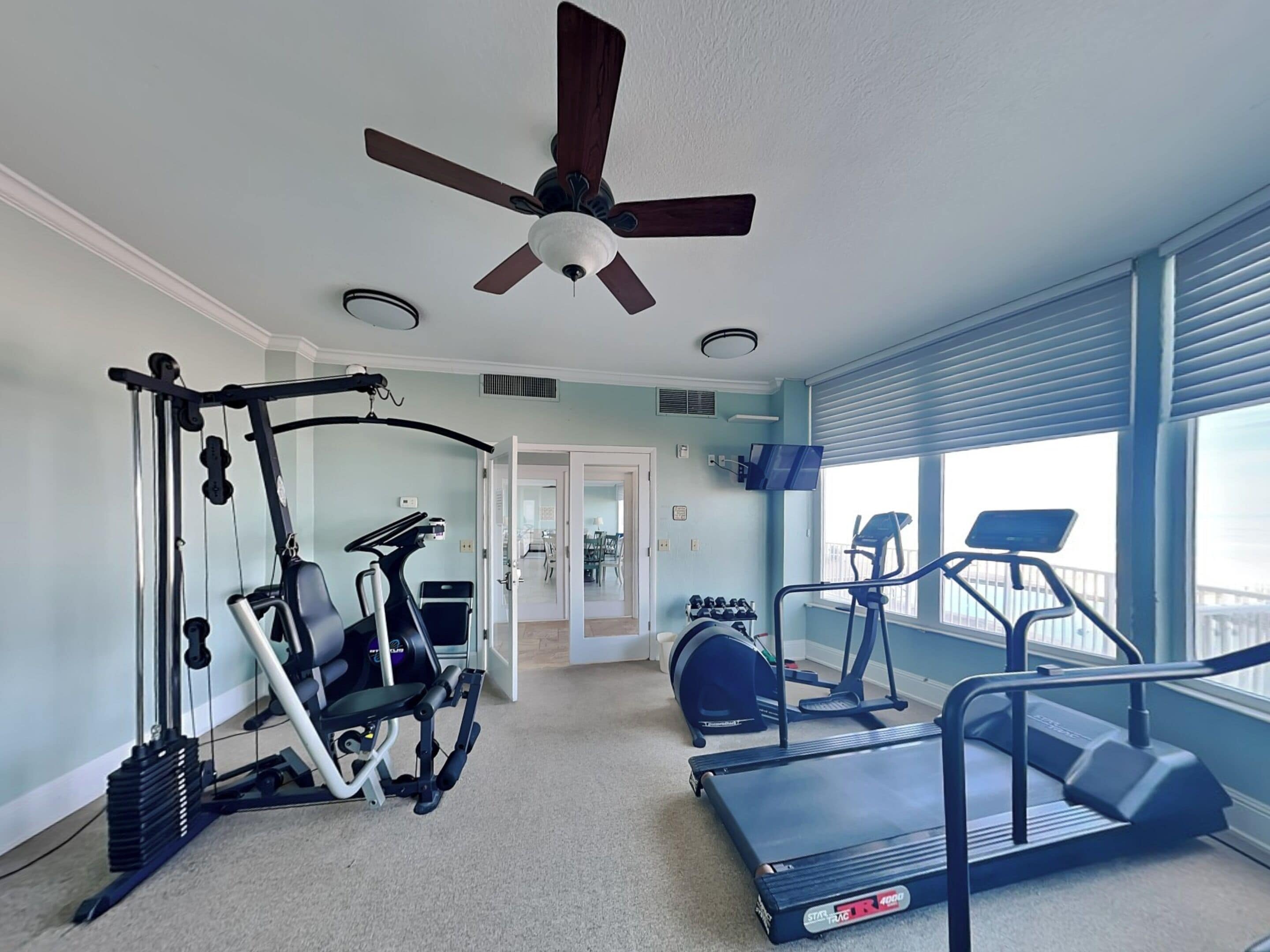 A home gym with a ceiling fan, treadmills, a stationary bike, and a weight machine.