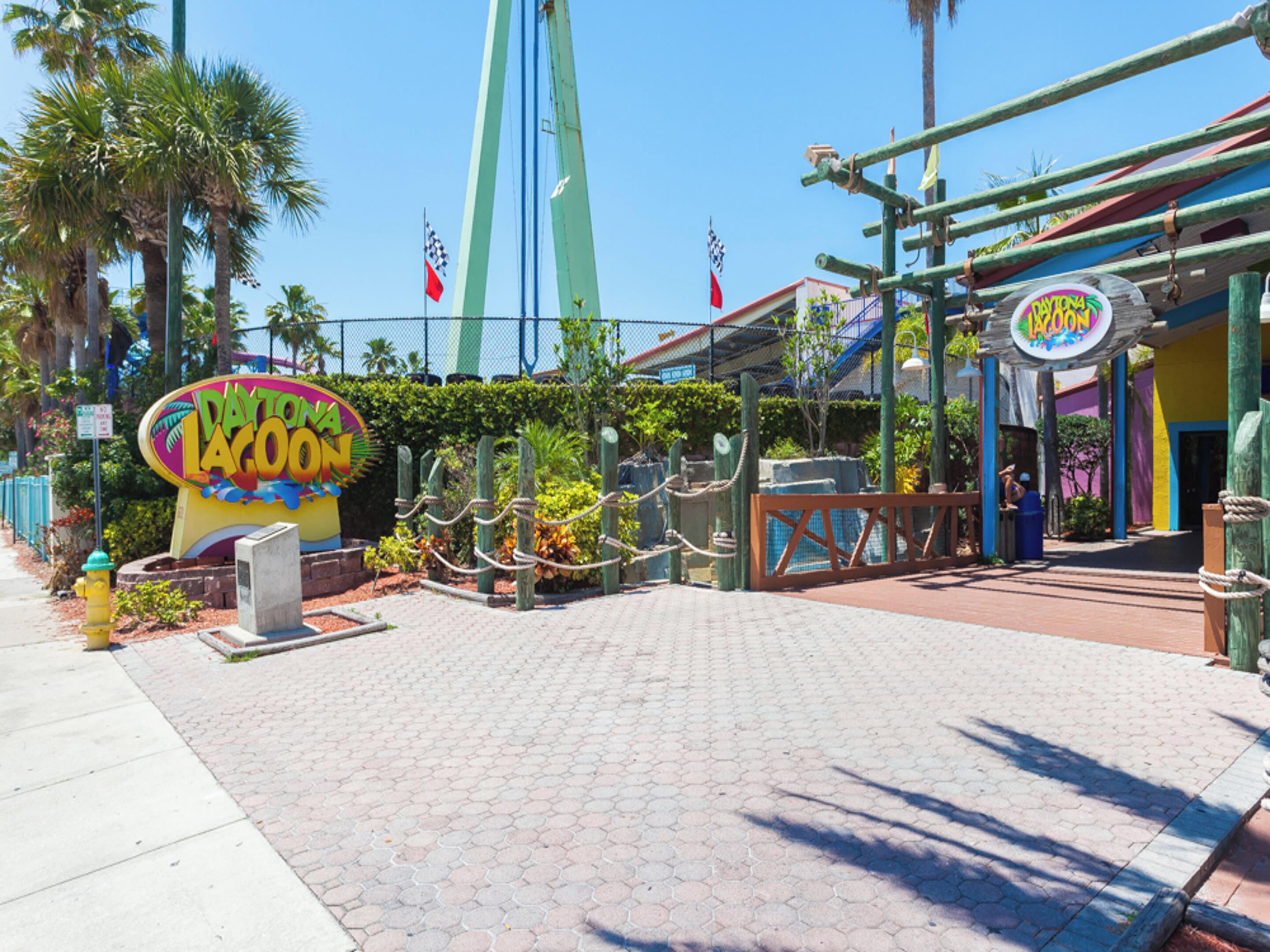 A paved entrance with a sign for Daytona LAGOON, palm trees, and a flag.