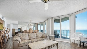Un salon spacieux avec un grand canapé d’angle beige, une table basse et un balcon offrant une vue sur l’océan.