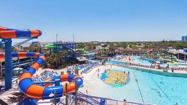 Un parc aquatique doté de nombreux toboggans et de plusieurs piscines, entouré d’espaces de plage et de chaises longues.