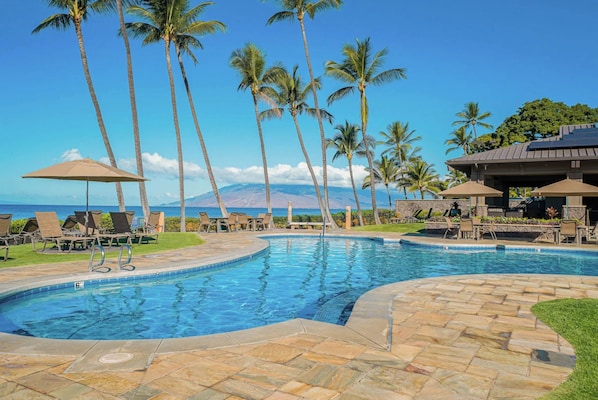 A swimming pool with lounge chairs and umbrellas, surrounded by palm trees and a view of the ocean. - Wailea Ekahi by Maui Rental Group (Kihei)