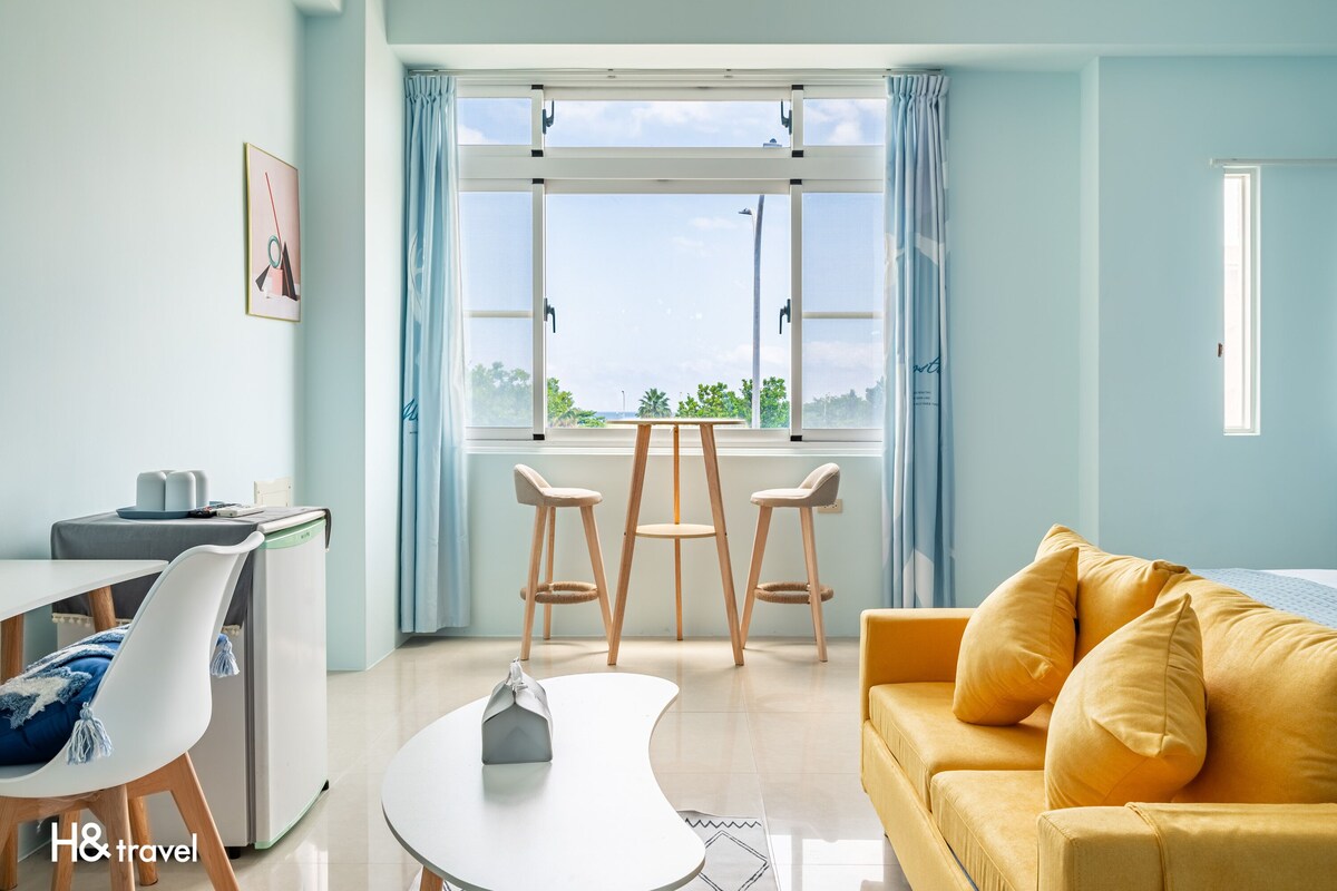 A modern living room with a yellow sofa, a white coffee table, and a dining area with a small table and chairs.
