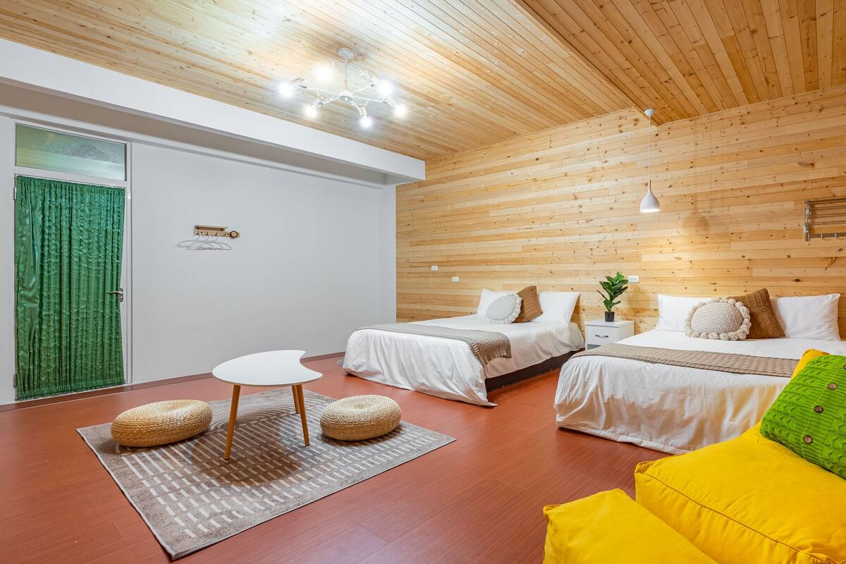 A room with two beds, a small table, and a green and yellow sofa.