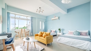 A modern hotel room with a yellow sofa, a white bed, and a dining area with a table and chairs.