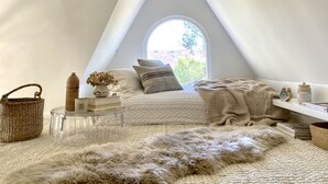 A cozy, well-lit room with a sloped ceiling, a clear glass table, a fluffy rug, and a comfortable seating area with pillows and a knitted blanket. - THE Zen Treehouse Retreat- Great Views and Peaceful Decks!
 (Los Angeles)
