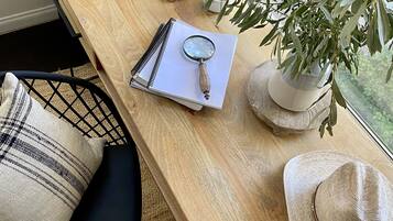A wooden desk with a notebook, magnifying glass, and a hat. A plant and a picture frame are also visible.
