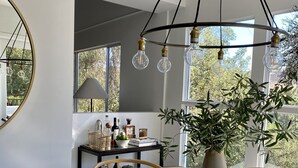 Un espace repas moderne avec une table ronde, des chaises en bois, un vase avec une plante et un luminaire suspendu.