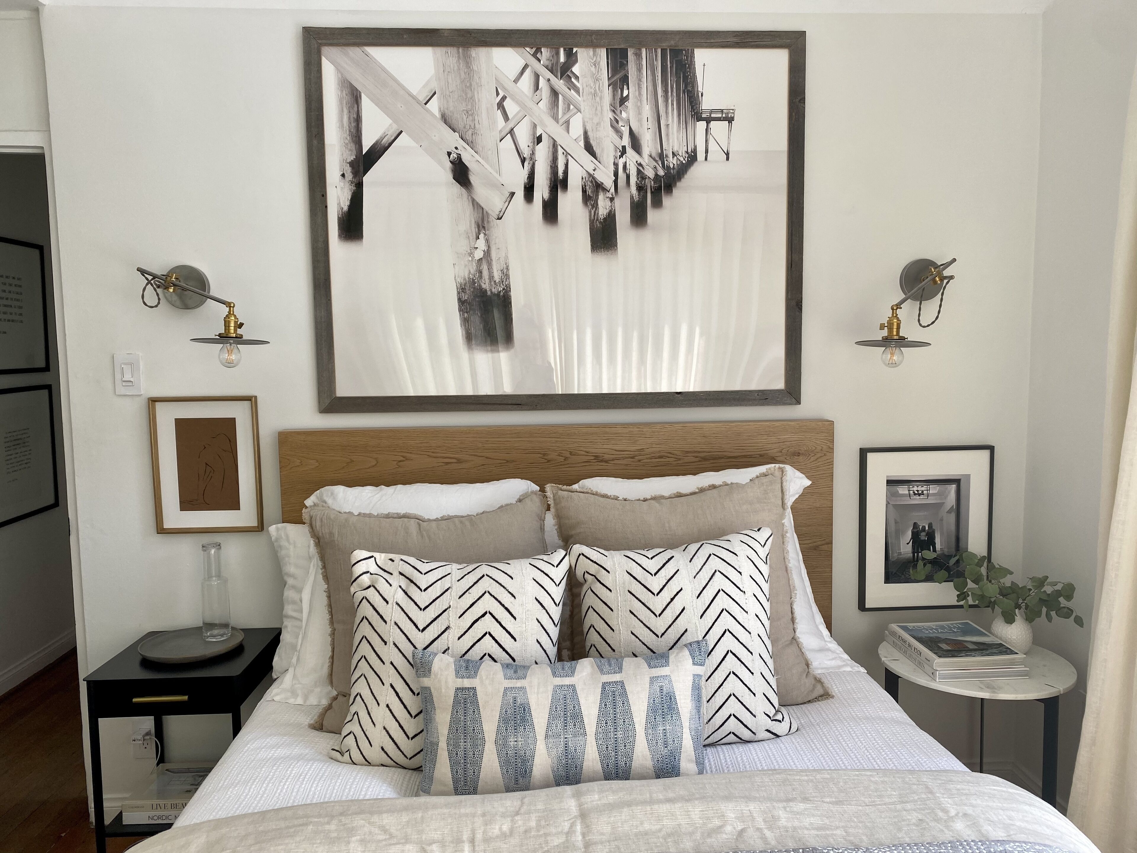 Une chambre à coucher bien aménagée, avec un grand tableau abstrait, une tête de lit en bois et une table de chevet sur laquelle sont posés des livres et une lampe.