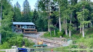 A lakeside cabin with a deck, dock, and boats. - All-Season Family Retreat • Hot Tub • Waterfront (Moyie)